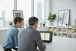 Happy graphic designer and client with their backs to the camera, looking at a laptop in a modern graphic design studio with the Menu on the screen. View shows the screen with the menu in an application